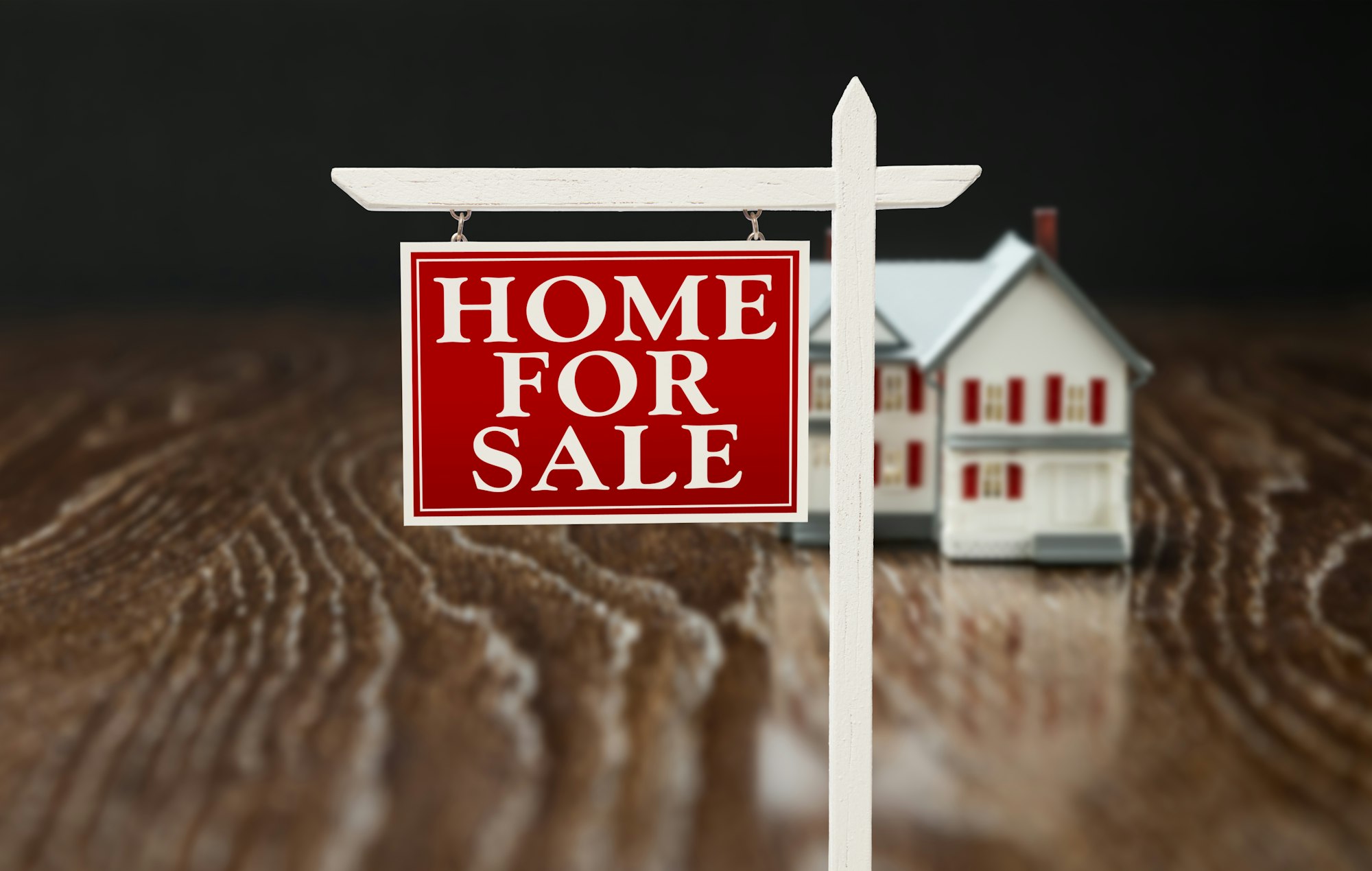 For Sale Real Estate Sign In Front of Model Home on Reflective Wooden Surface.